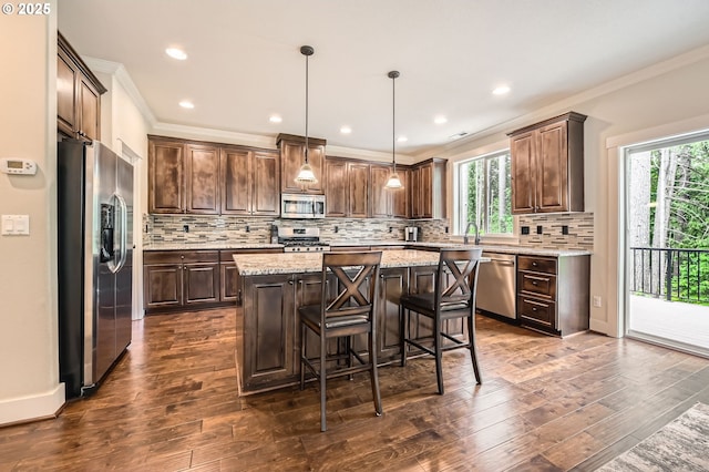 kitchen featuring stainless steel appliances, a center island, crown molding, healthy amount of natural light, and dark wood finished floors