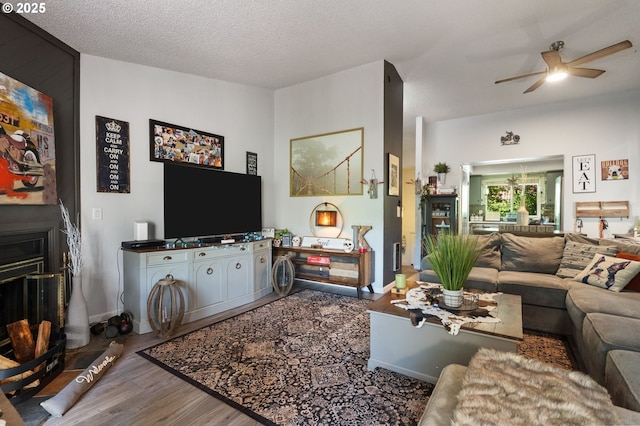 living area featuring baseboards, ceiling fan, a fireplace, wood finished floors, and a textured ceiling