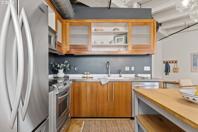 kitchen with stainless steel appliances, brown cabinetry, a sink, and glass insert cabinets