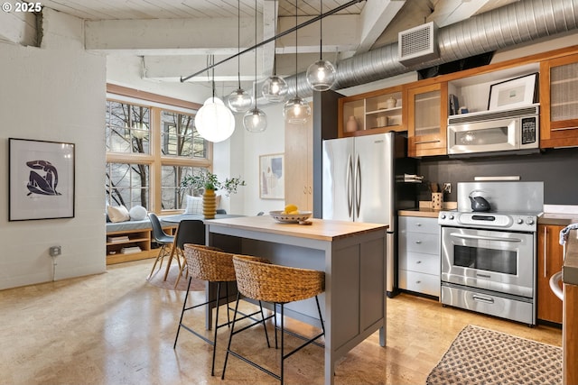 kitchen featuring stainless steel appliances, a breakfast bar, butcher block counters, and brown cabinetry