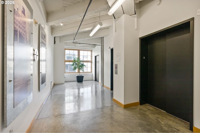 corridor featuring elevator, beamed ceiling, finished concrete flooring, and baseboards