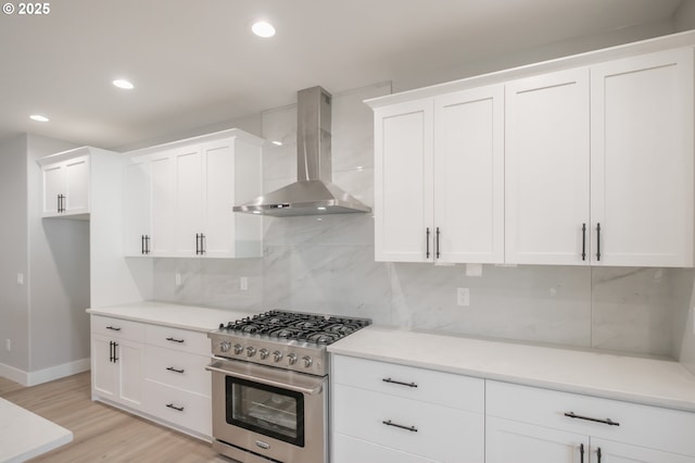 7320 Tanglewood Ave, Gleneden Beach, OR 97388 - kitchen featuring wall chimney range hood, stainless steel stove, white cabinetry, light wood-style floors, and decorative backsplash