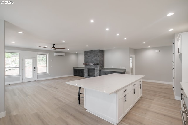 7320 Tanglewood Ave, Gleneden Beach, OR 97388 - kitchen featuring a fireplace, ceiling fan, a center island, white cabinetry, and light wood finished floors