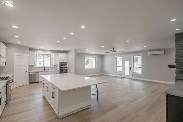 7320 Tanglewood Ave, Gleneden Beach, OR 97388 - kitchen with a wall mounted AC, appliances with stainless steel finishes, a kitchen island, white cabinets, and a ceiling fan