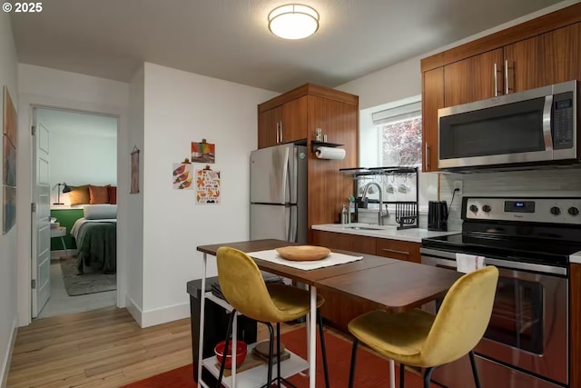 kitchen featuring light wood finished floors, brown cabinetry, appliances with stainless steel finishes, a kitchen bar, and a sink