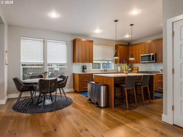 kitchen featuring stainless steel microwave, brown cabinetry, backsplash, and light countertops