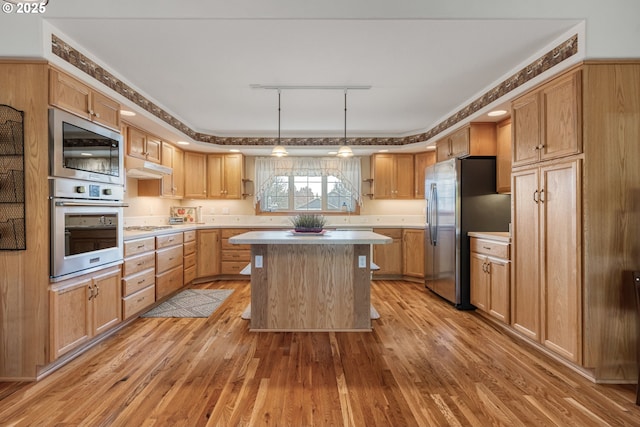 kitchen with under cabinet range hood, stainless steel appliances, light wood-style floors, light countertops, and a center island