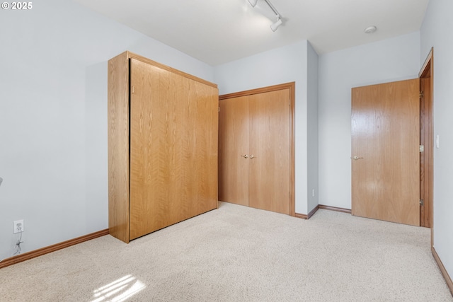 unfurnished bedroom with carpet, a closet, baseboards, and track lighting