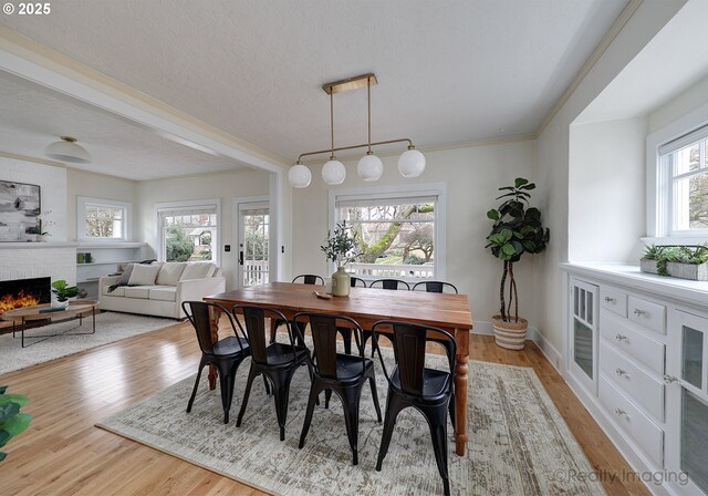 dining room featuring a textured ceiling, light hardwood / wood-style floors, a brick fireplace, and plenty of natural light