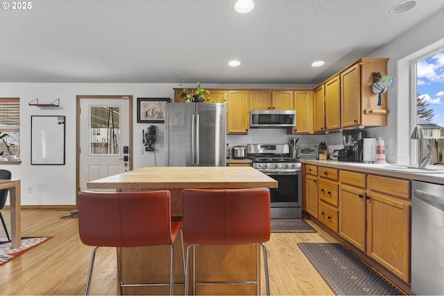 kitchen with light wood-type flooring, a sink, a center island, recessed lighting, and stainless steel appliances