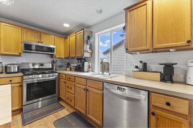 kitchen with a sink, light wood finished floors, appliances with stainless steel finishes, and light countertops