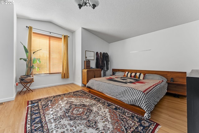 bedroom featuring a textured ceiling, wood finished floors, baseboards, and vaulted ceiling