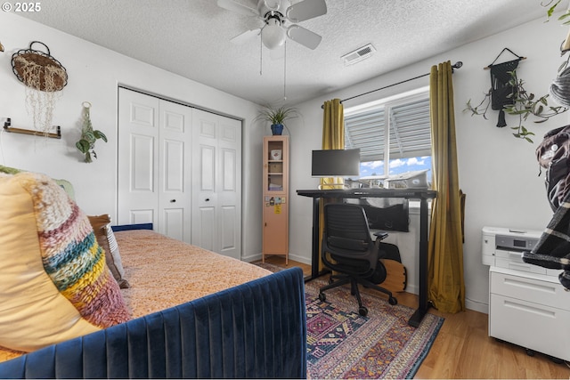 bedroom with light wood finished floors, visible vents, ceiling fan, a closet, and a textured ceiling