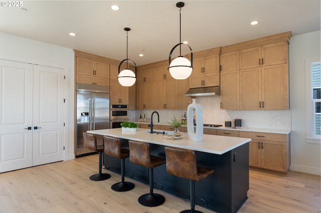 kitchen with stainless steel appliances, light countertops, decorative backsplash, light wood-style floors, and under cabinet range hood