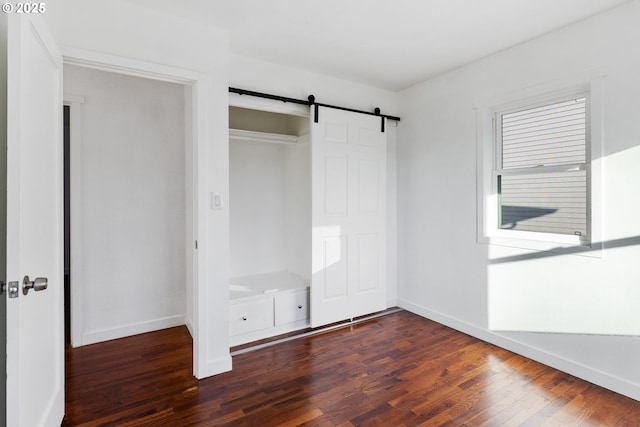 unfurnished bedroom with a closet, dark hardwood / wood-style floors, and a barn door