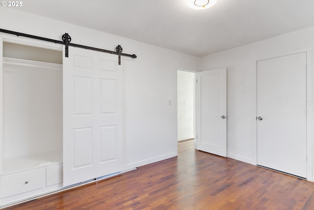 unfurnished bedroom featuring a barn door, dark wood-type flooring, and a closet