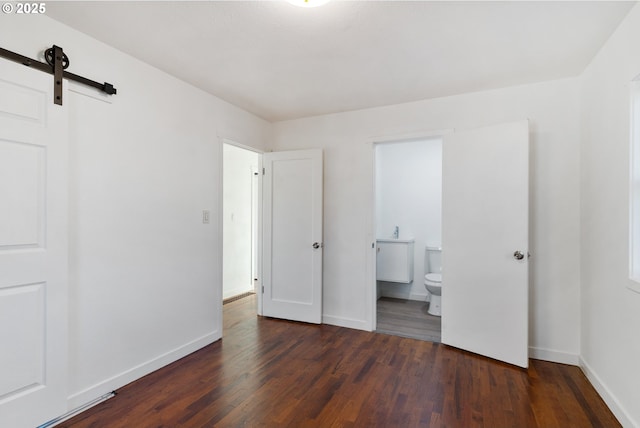 unfurnished bedroom with ensuite bathroom, a barn door, and dark wood-type flooring