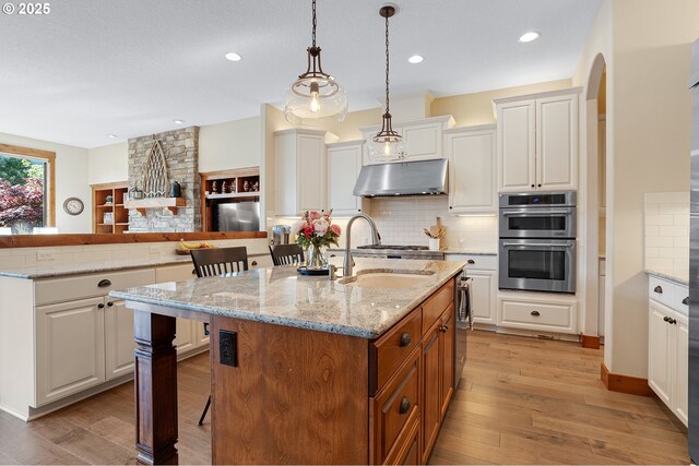 kitchen with light wood-type flooring, a sink, under cabinet range hood, and stainless steel appliances