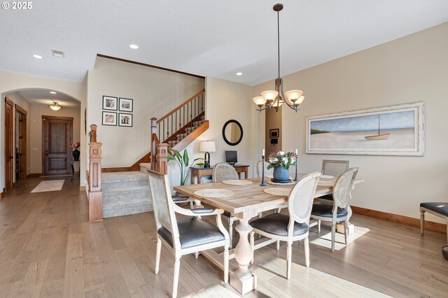 dining area featuring stairs, arched walkways, baseboards, and light wood-style flooring