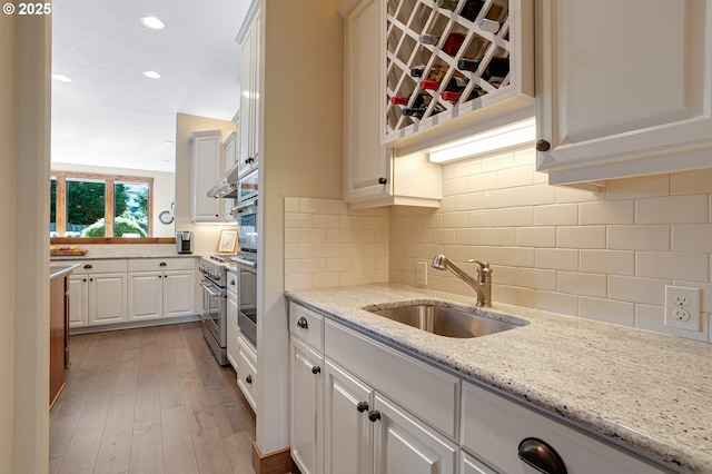 kitchen featuring white cabinetry, a sink, light wood finished floors, and tasteful backsplash