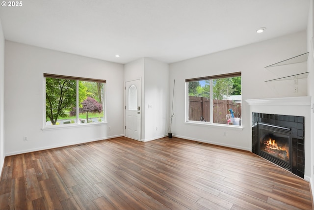 unfurnished living room with plenty of natural light, a fireplace, wood finished floors, recessed lighting, and baseboards