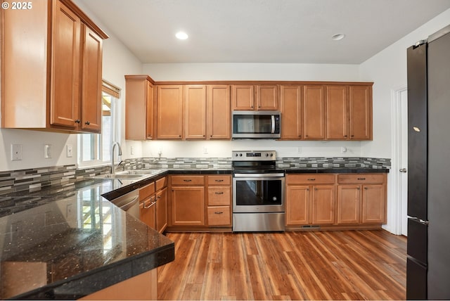 kitchen with appliances with stainless steel finishes, a sink, light wood-style floors, brown cabinets, and recessed lighting