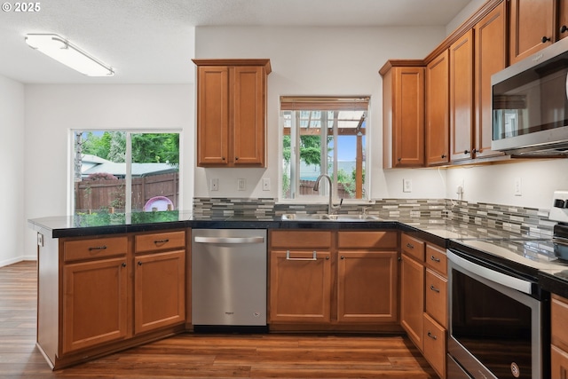 kitchen with appliances with stainless steel finishes, a sink, plenty of natural light, and brown cabinets