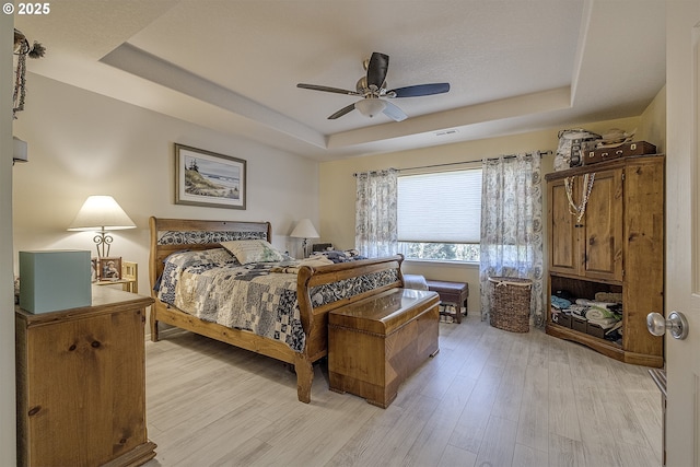 bedroom with light wood-style floors, a raised ceiling, visible vents, and ceiling fan