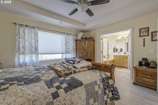 bedroom featuring a tray ceiling, visible vents, light wood-style floors, ceiling fan, and ensuite bath