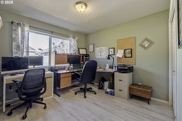 office space featuring a textured ceiling, baseboards, and light wood-style floors