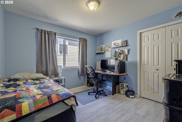 bedroom with a textured ceiling, wood finished floors, visible vents, baseboards, and a closet