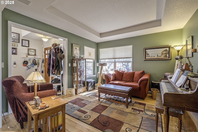 living room featuring light wood-style flooring, a tray ceiling, and a textured ceiling