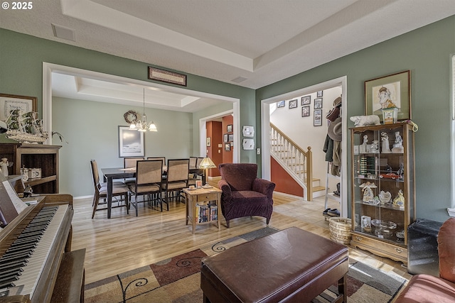 living room featuring a notable chandelier, light wood finished floors, a raised ceiling, baseboards, and stairs