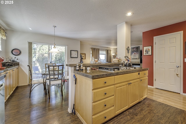 kitchen featuring dark wood-style floors, stainless steel appliances, a textured ceiling, light brown cabinets, and pendant lighting