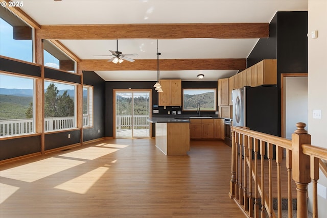 kitchen with wood finished floors, a ceiling fan, dark countertops, beam ceiling, and appliances with stainless steel finishes