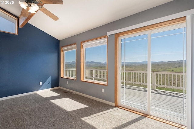 empty room featuring a mountain view, vaulted ceiling, carpet floors, a ceiling fan, and baseboards
