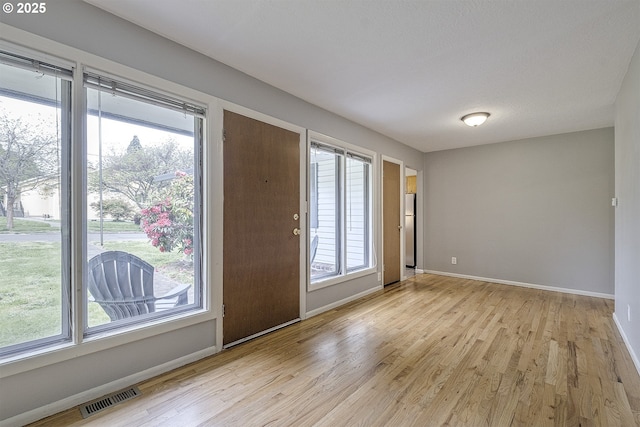 empty room featuring light wood-type flooring, baseboards, and plenty of natural light
