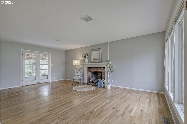 unfurnished living room with light wood finished floors, a brick fireplace, baseboards, and french doors