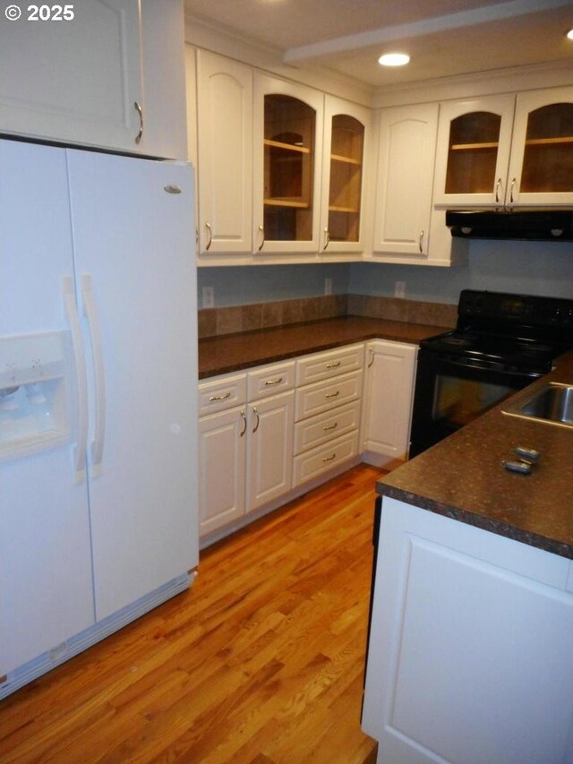 kitchen with black range with electric cooktop, dark countertops, white refrigerator with ice dispenser, under cabinet range hood, and light wood-style flooring