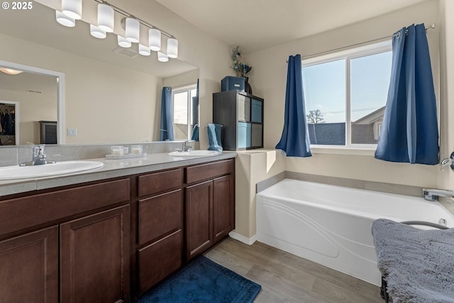 bathroom featuring double vanity, a garden tub, a sink, and wood finished floors