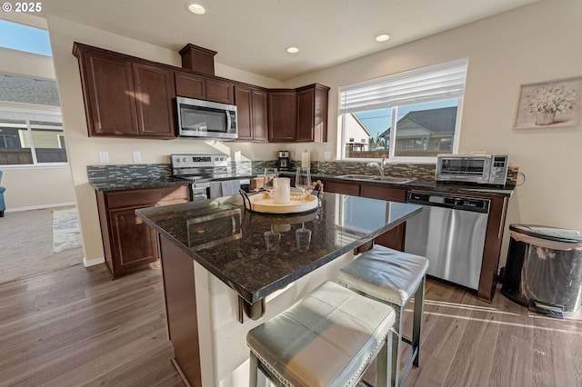 kitchen featuring recessed lighting, a toaster, stainless steel appliances, a sink, and dark stone counters