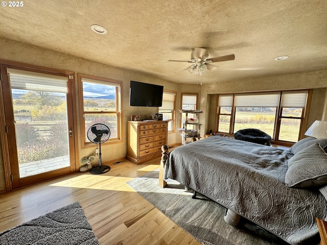 bedroom featuring access to exterior, ceiling fan, light hardwood / wood-style floors, and a textured ceiling