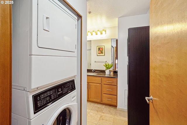 laundry area featuring a textured ceiling, laundry area, a sink, and stacked washer / drying machine