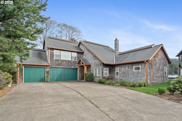 view of front facade with concrete driveway, a garage, roof with shingles, and a chimney