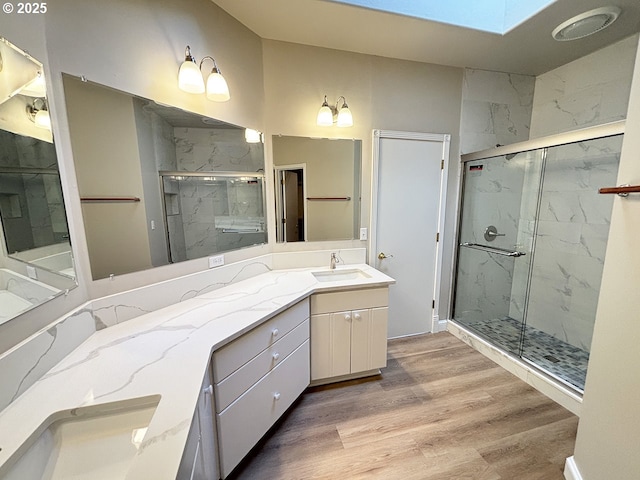 full bath with a skylight, vanity, a marble finish shower, and wood finished floors