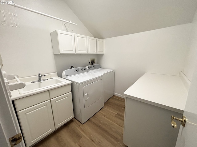 washroom featuring washing machine and dryer, cabinet space, a sink, and wood finished floors