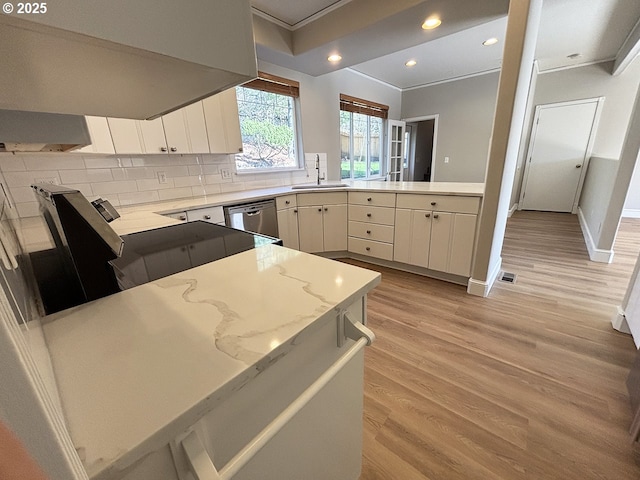 kitchen with a peninsula, range hood, light wood-type flooring, decorative backsplash, and dishwasher