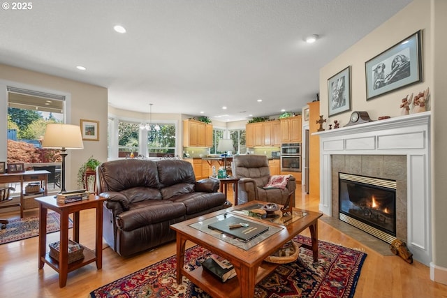 living room with recessed lighting, a tiled fireplace, and light wood-style floors