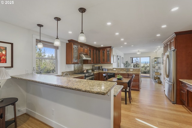 kitchen featuring a kitchen breakfast bar, appliances with stainless steel finishes, light wood-type flooring, kitchen peninsula, and pendant lighting