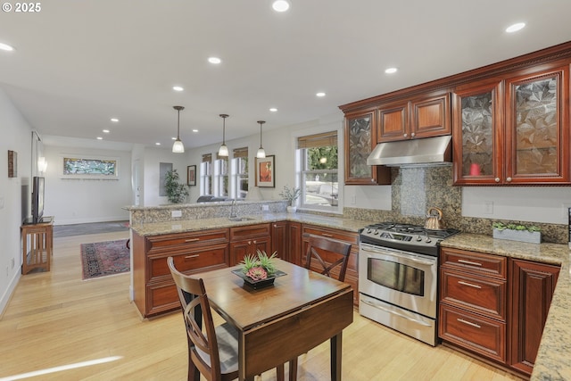 kitchen featuring light wood-type flooring, kitchen peninsula, stainless steel gas range oven, decorative backsplash, and hanging light fixtures